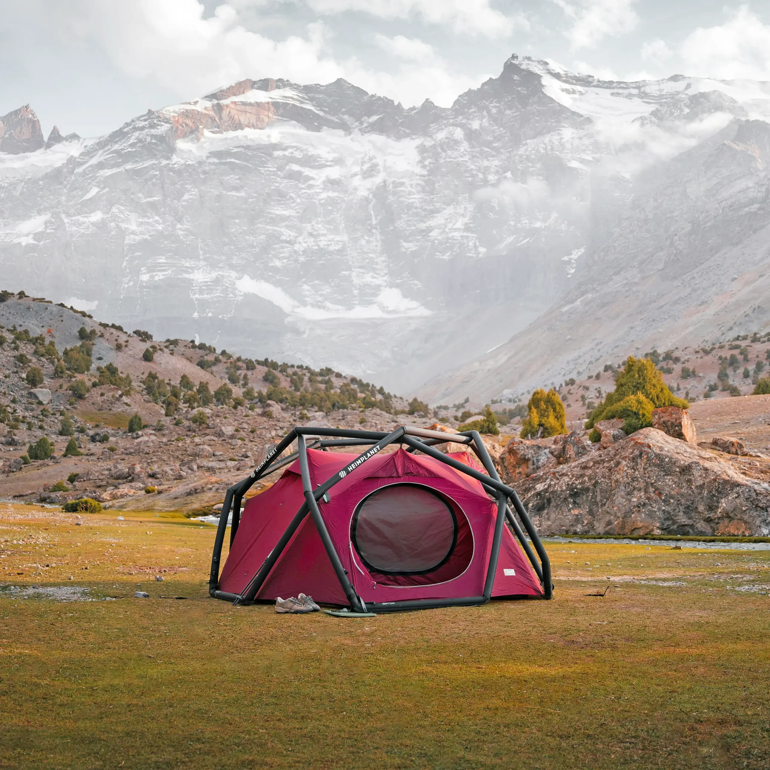 Red tent on the grass with hills and a snowy mountain in the background.