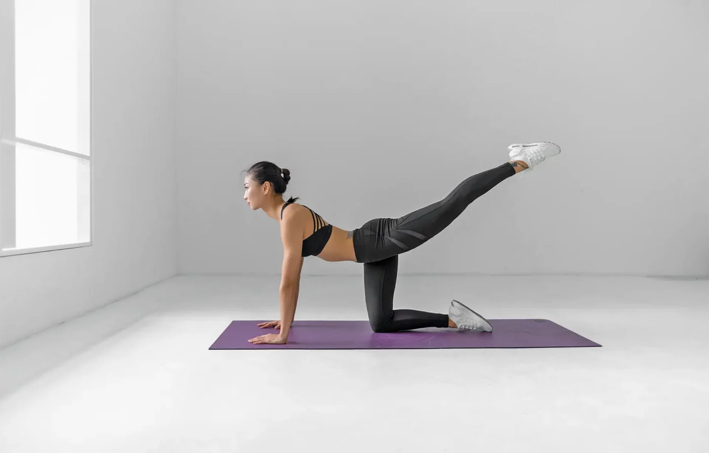 Young woman doing Pilates on a purple mat in an empty white room.