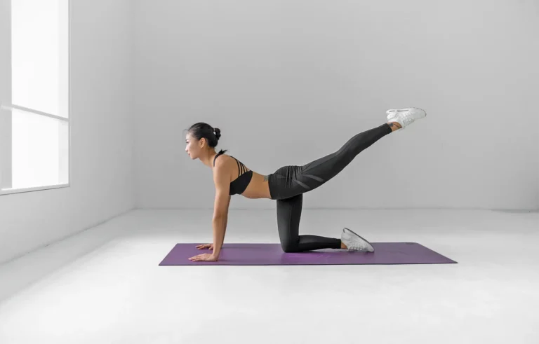 Young woman doing Pilates on a purple mat in an empty white room.