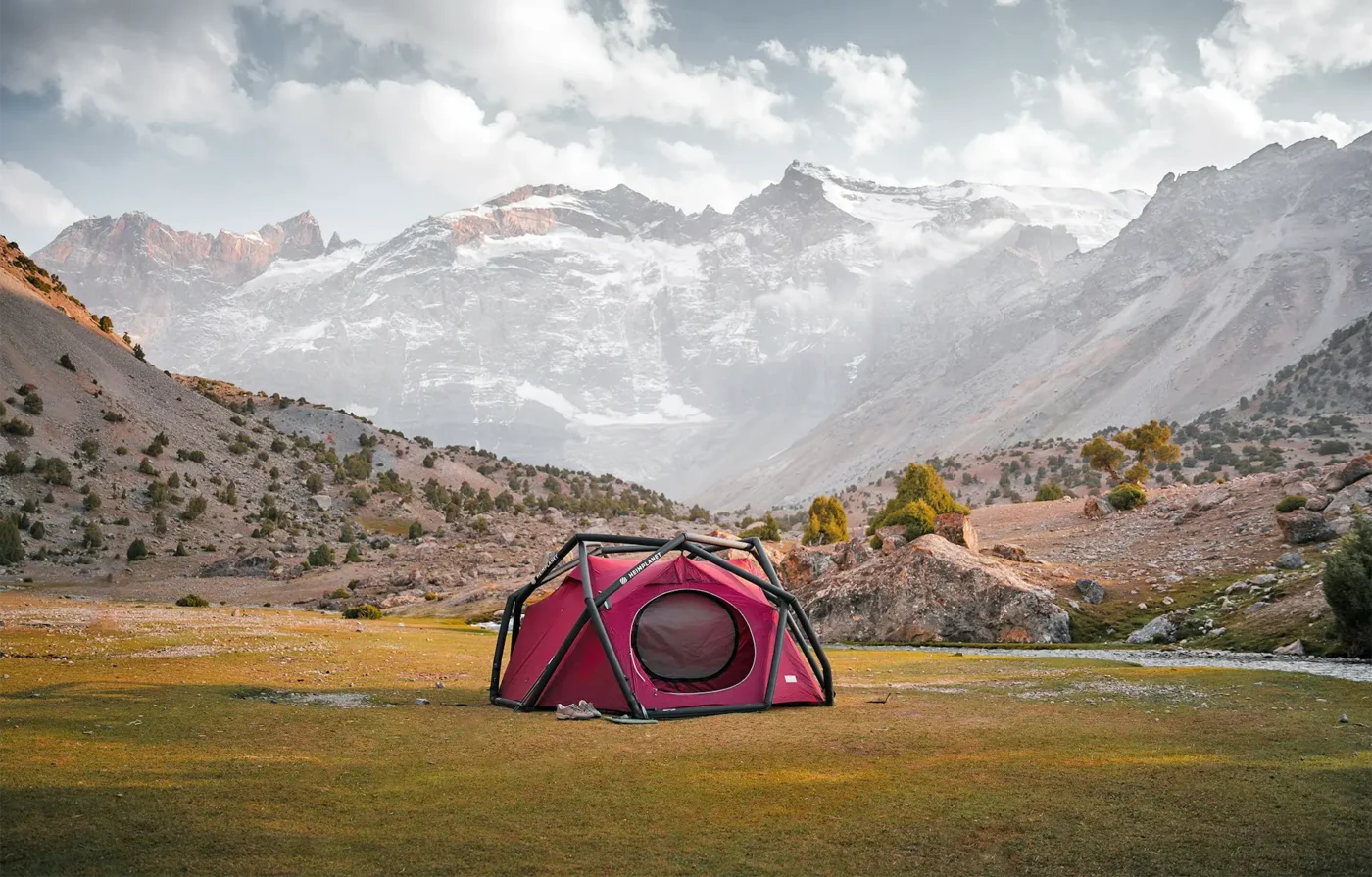 Red tent on the grass with hills and a snowy mountain in the background.