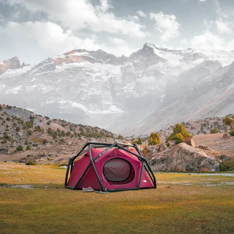 Red tent on the grass with hills and a snowy mountain in the background.